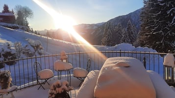 A snow-covered outdoor seating area with chairs and a fence, overlooking a mountainous landscape.