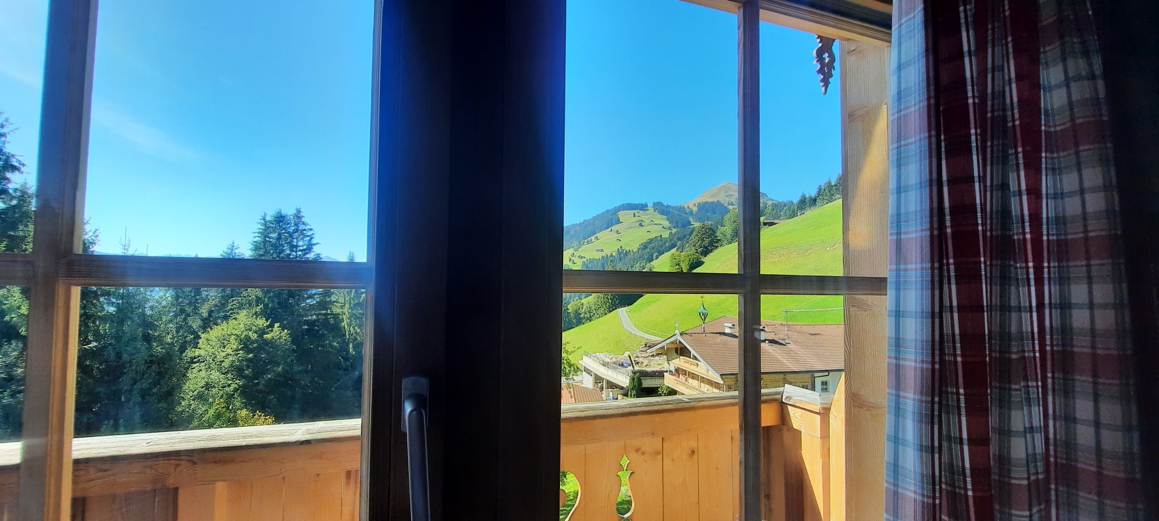 Una ventana con vistas a un paisaje verde, una estructura de madera y una montaña al fondo.