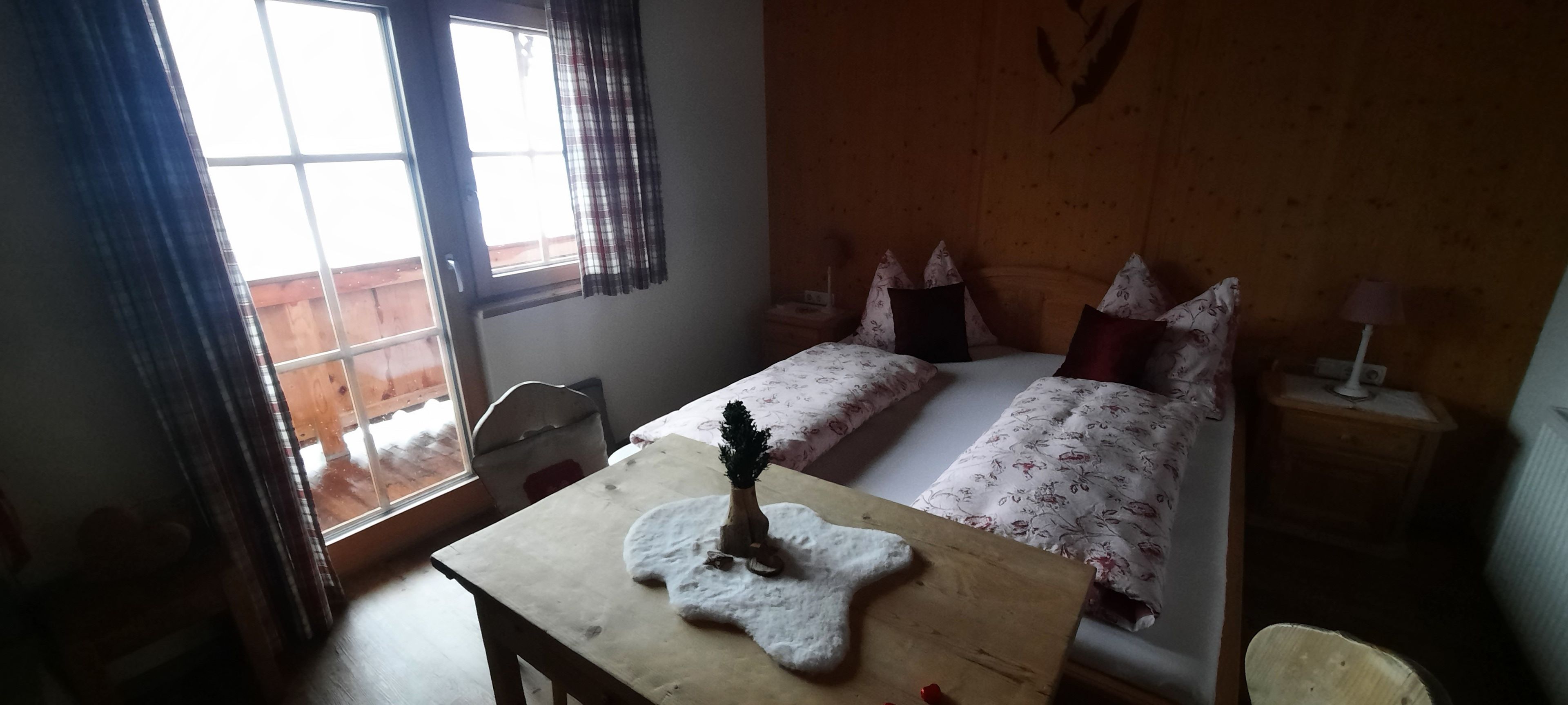 Une chambre avec deux lits, une tête de lit en bois, une petite table ornée d’un objet décoratif et une fenêtre avec des rideaux.