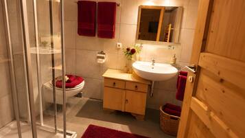 Een moderne badkamer met een douchecabine van glas, een houten wastafelmeubel, een witte wastafel en een rode badmat.