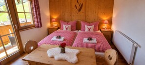 A room with a bed, two bedside tables, a wooden table, a chair, and a window with curtains. - Room 'Bergpension Ebental Zimmer 4' with Mountain View, Shared Terrace and Wi-Fi (Brixen im Thale)