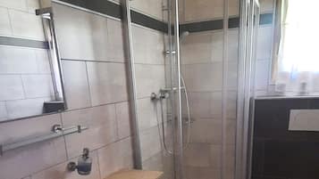 Ein Badezimmer mit einem weißen Waschbecken, einem Holzkorpus, einer Duschkabine aus Glas und einer Toilette.
