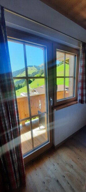 A room with a large sliding glass door leading to an outdoor balcony with a view of a green landscape. - Room 'Bergpension Ebental Zimmer 4' with Mountain View, Shared Terrace and Wi-Fi (Brixen im Thale)