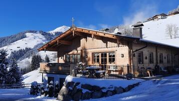 Eine Holzchalet mit Balkon, umgeben von schneebedeckten Bäumen und Bergen.