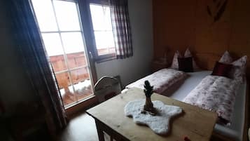 A room with two beds, a wooden headboard, a small table with a decorative item, and a window with curtains.