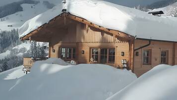 Un chalet en bois doté d’un toit en pente, entouré d’un paysage enneigé et de montagnes.