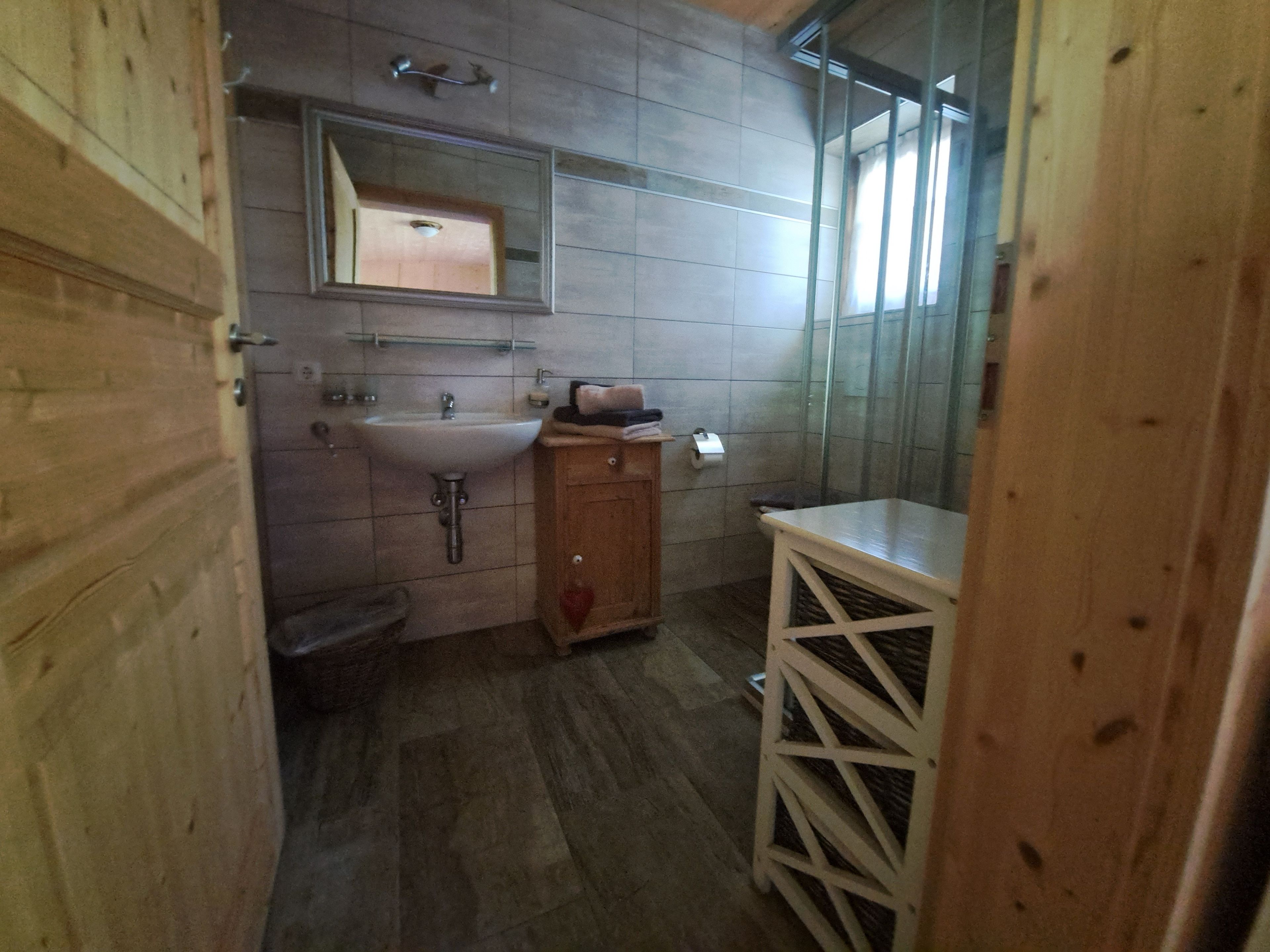 Ein Badezimmer mit Holzboden, Waschbecken, Spiegel und Duschbereich.