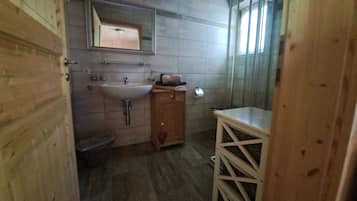 Ein Badezimmer mit Holzboden, Waschbecken, Spiegel und Duschbereich.