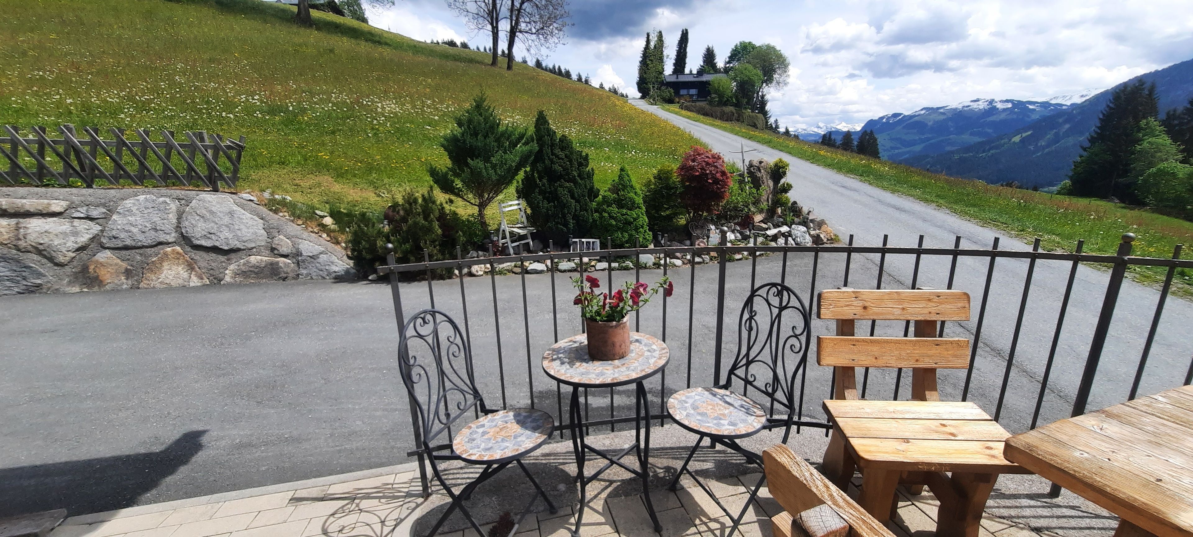 Ein reizvoller Außenbereich mit Sitzgelegenheiten, einem Tisch, Stühlen, einem Blumentopf und Blick auf eine Bergstraße.
