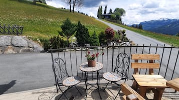Ein reizvoller Außenbereich mit Sitzgelegenheiten, einem Tisch, Stühlen, einem Blumentopf und Blick auf eine Bergstraße.