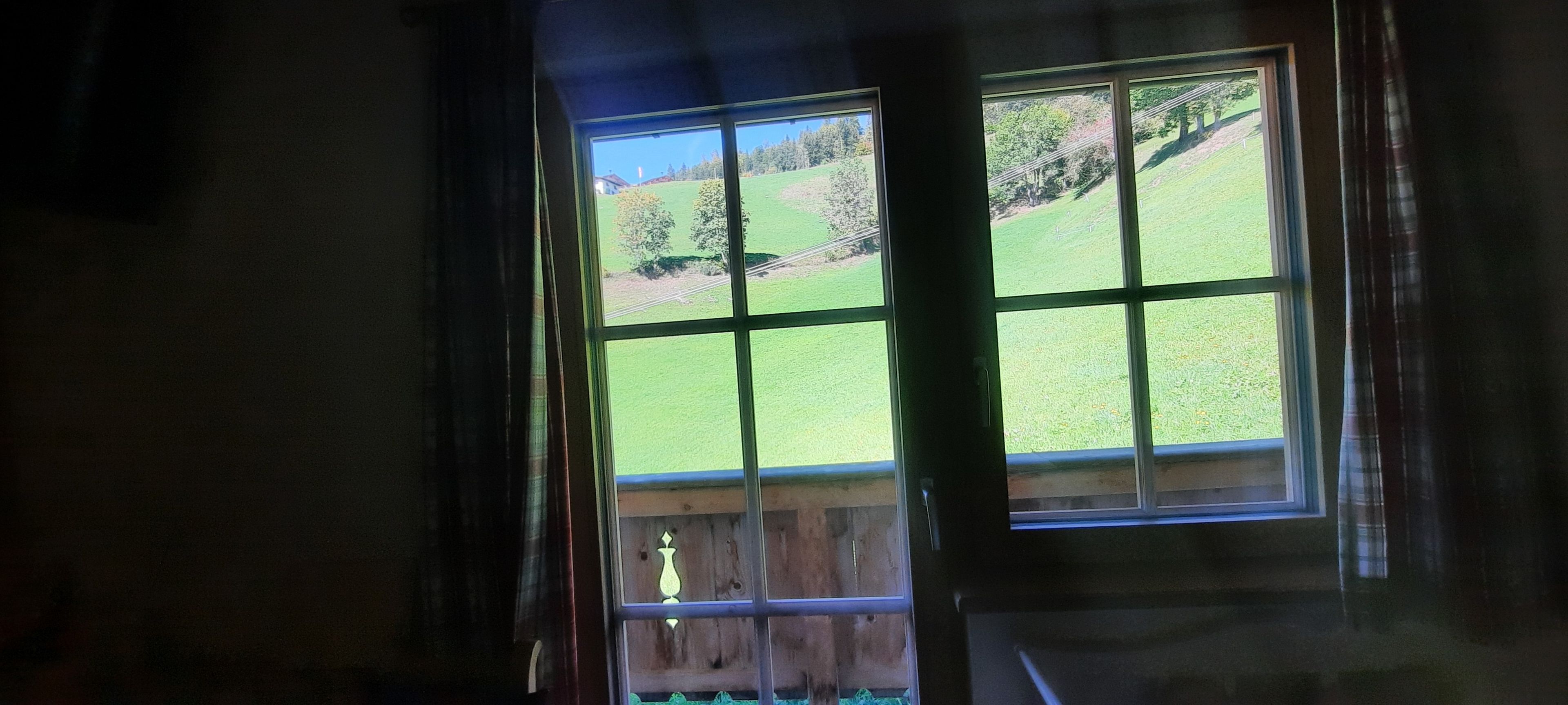 Finestra amb vista a un paisatge verd, cortines entreobertes i una estructura de fusta a la part inferior.