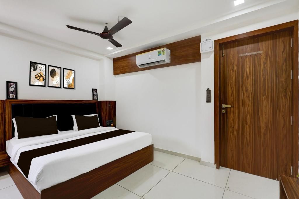 Un dormitorio con cama, ventilador de techo, aire acondicionado, puerta de madera y cuadros en la pared.