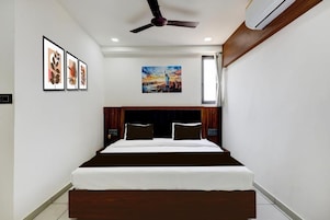 A hotel room with a bed, ceiling fan, artwork on the wall, and an air conditioning unit.