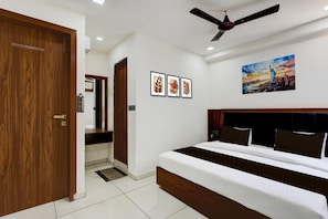 A bedroom with a bed, a ceiling fan, and wall art. - HOTEL SHUBH SANKALP (Sanand)