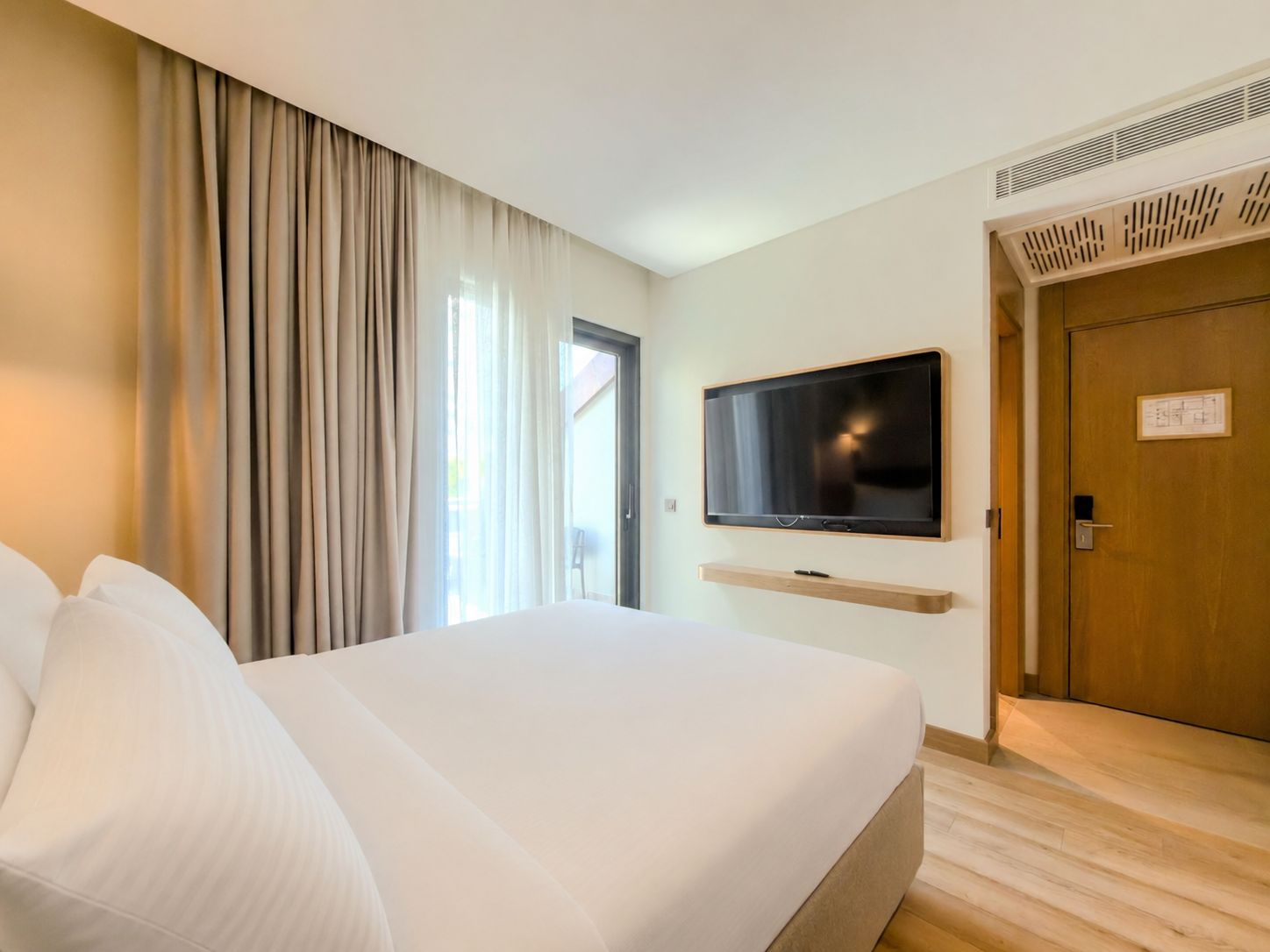 Una habitación de hotel con una cama grande, un televisor montado en la pared y una puerta con un cartel.