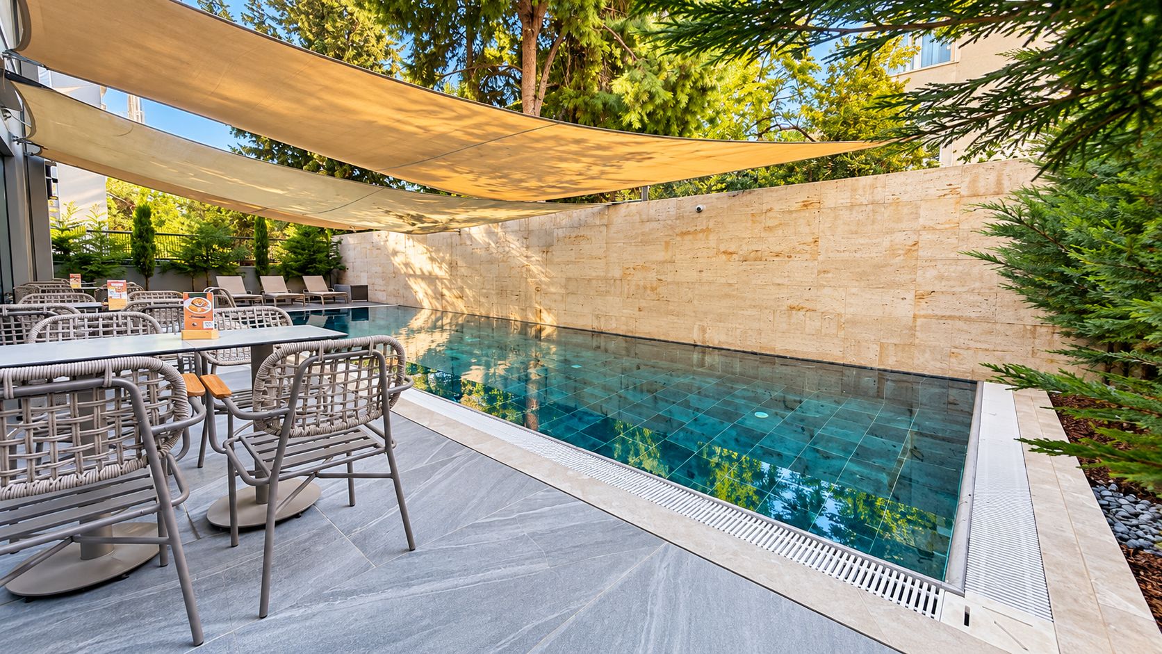 Piscina exterior con pared de piedra, rodeada de mobiliario de exterior y cubierta por una marquesina.