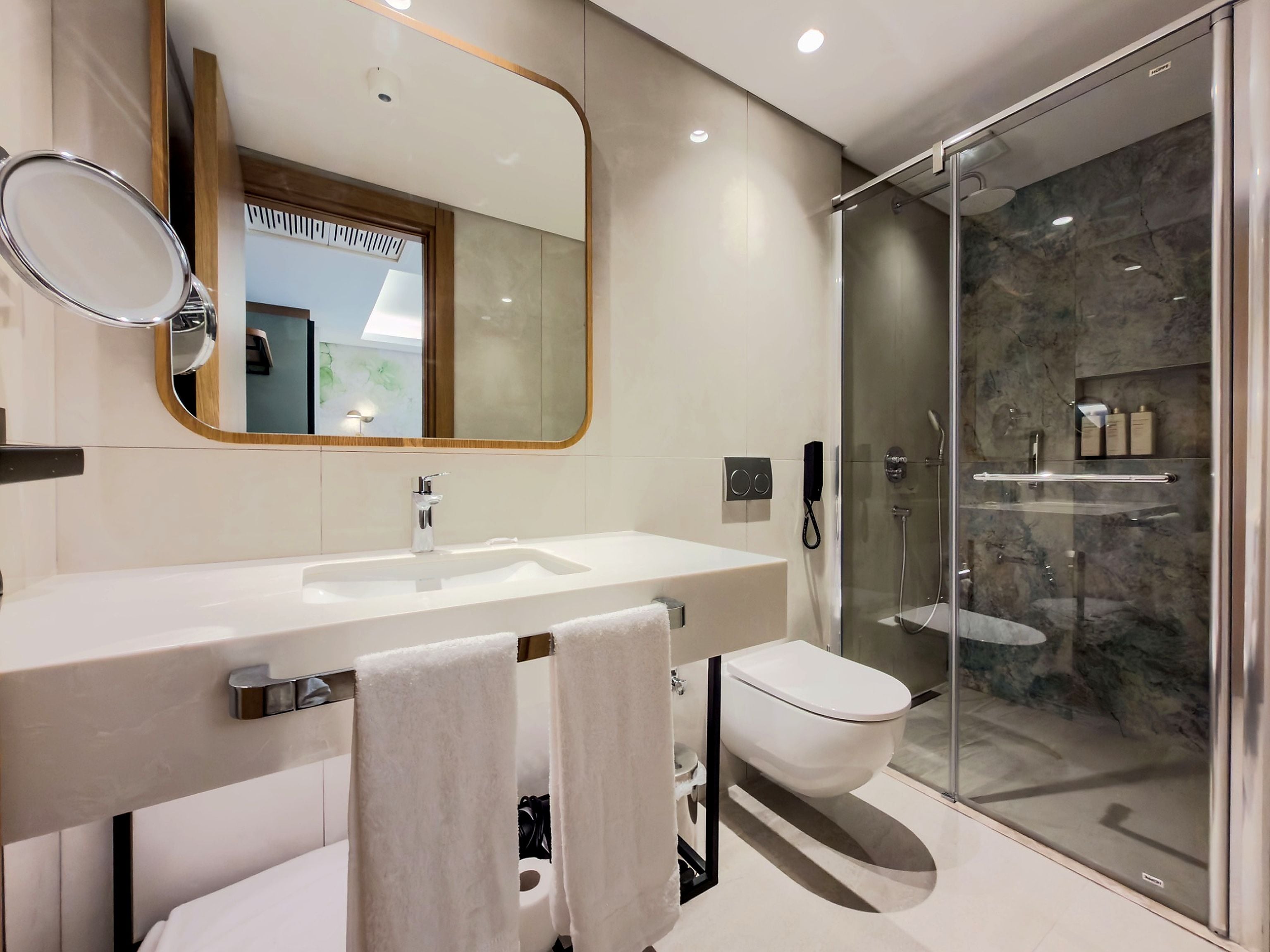 Un baño moderno con un espejo grande, un lavamanos, un inodoro y una zona de ducha con mampara de vidrio.