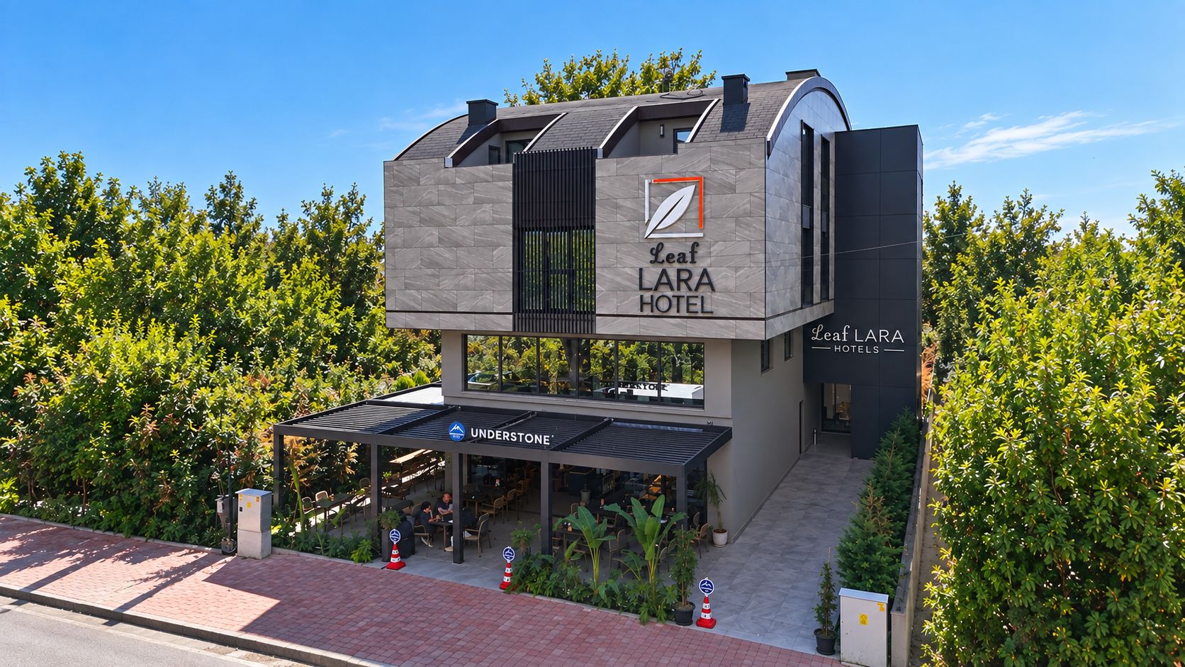 Un moderno edificio de hotel con techo plano, un área de estar al aire libre cubierta y un letrero del Hotel Leaf LARA.