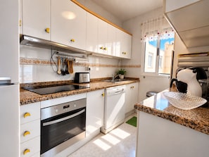 Une cuisine moderne avec des meubles blancs, un four encastré, un lave-vaisselle et un plan de travail sur lequel se trouve un grille-pain.