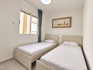 A room with two single beds, a window with curtains, and a wall-mounted painting. - Upper-floor Bungalow With Private Solarium and Community Pool in San Luis (Torrevieja)