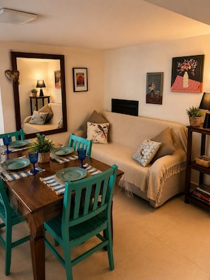 A cozy living room with a sofa, a dining table set with plates and glasses, and a bookshelf with books.