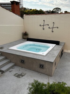 A hot tub on a concrete platform with steps leading up to it, a wall-mounted decorative metal piece, and a small potted plant. - Studio 442 (Águas de São Pedro)