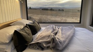 A bedroom with a large window, a bed with pillows, and a blanket.