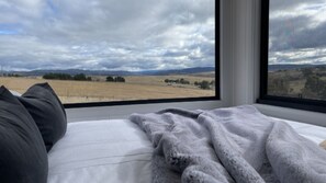 Ein Schlafzimmer mit einem großen Fenster und Blick auf ein Feld und ferne Berge.