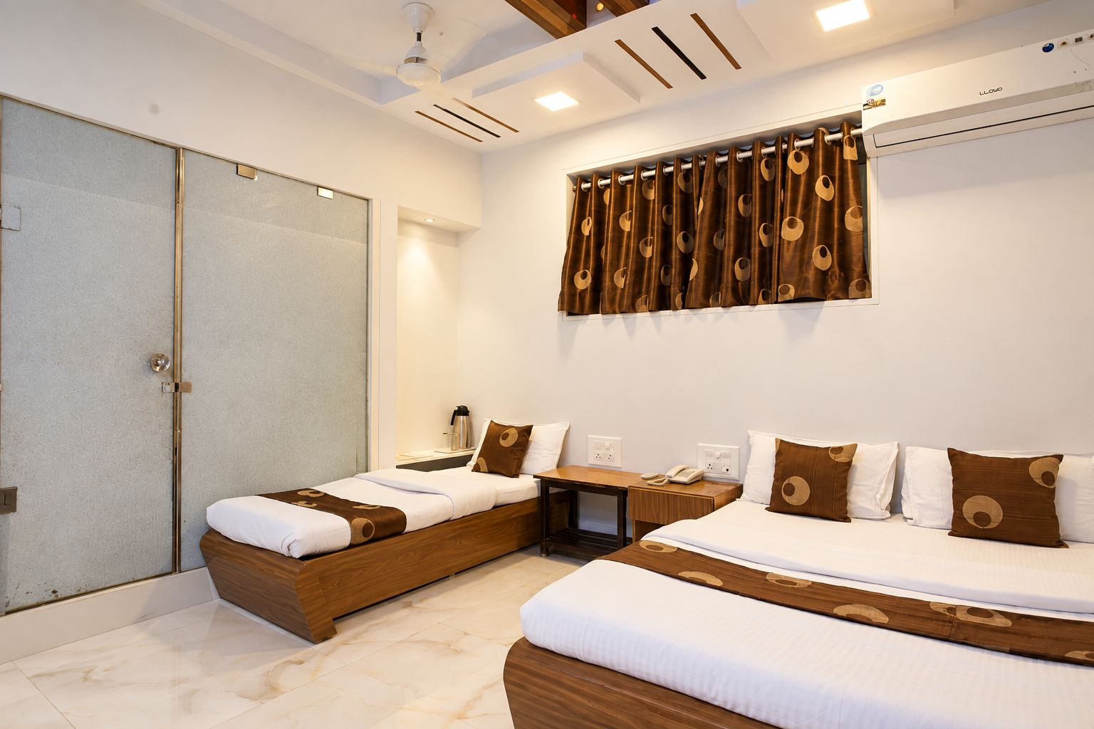 A hotel room with two beds, a desk, a wardrobe, and a ceiling fan.
