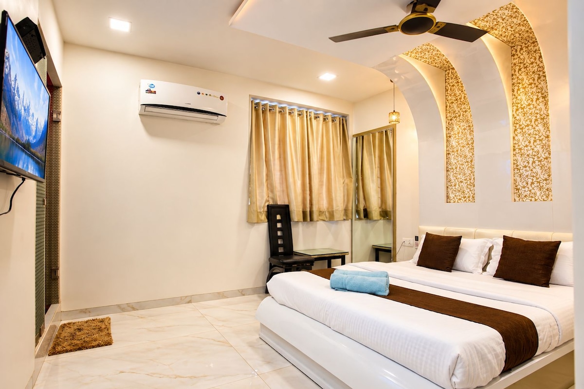 A hotel room with a bed, a television, an air conditioning unit, a ceiling fan, and a window with curtains.