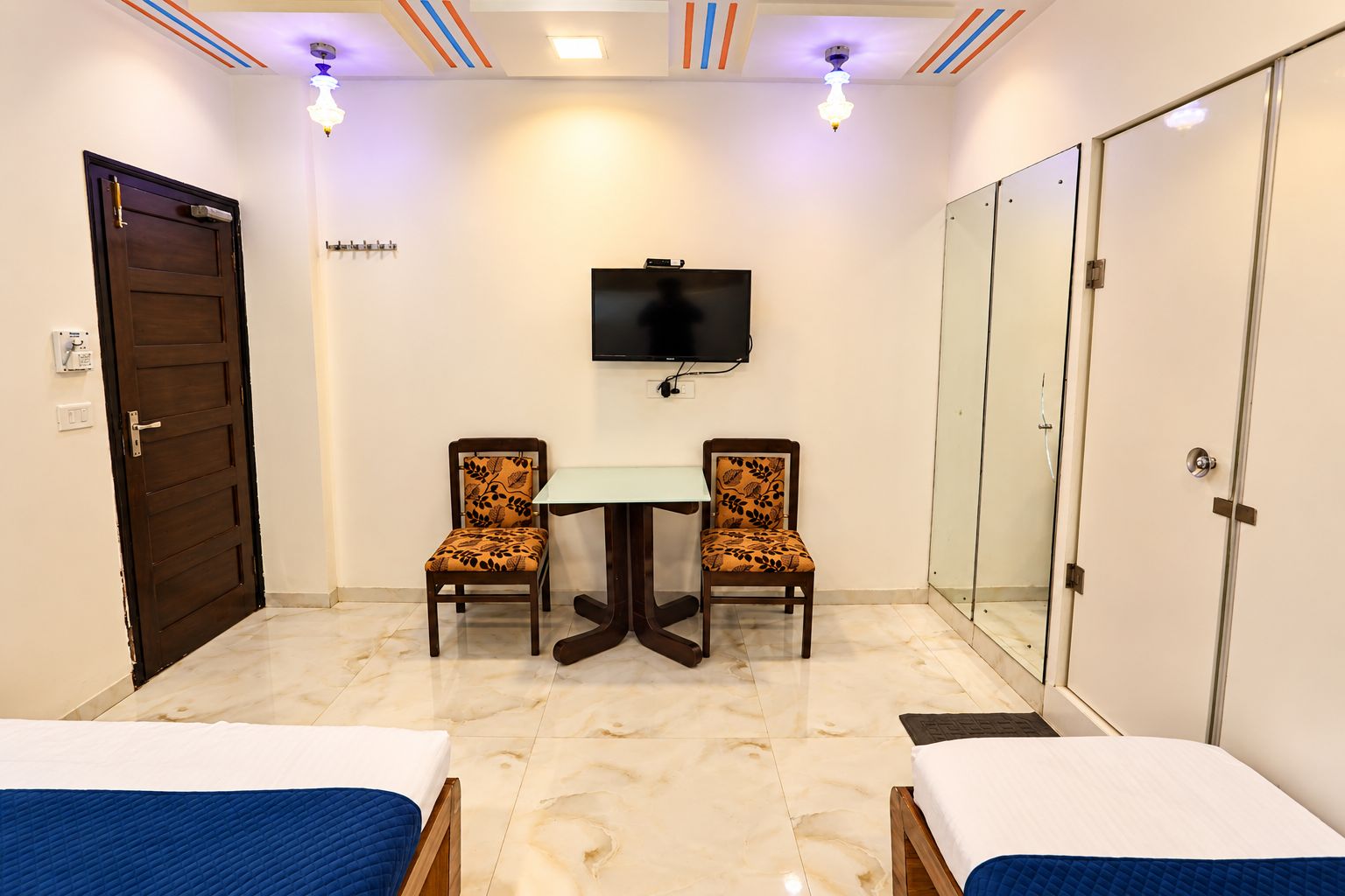 Habitación de hotel con cama, escritorio, dos sillas, televisor, armario y espejo.