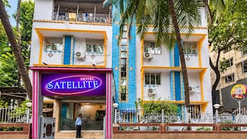 A hotel with a prominent neon sign, multiple balconies, and a gated entrance.