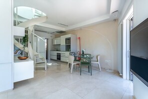 A modern kitchen with a spiral staircase, a dining area with a glass table, and a flat-screen TV. - iFlat | Spanish Steps Unique Panoramic Penthouse (Rome)