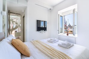 Une chambre d’hôtel avec un lit, une télévision, une fenêtre donnant sur la ville et une porte menant à un balcon.