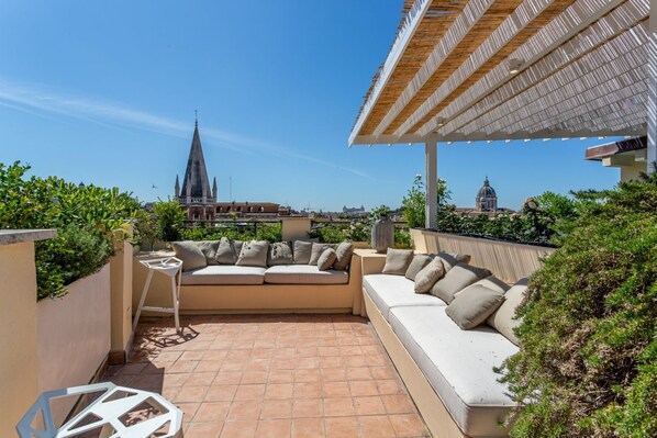 Un espace extérieur aménagé avec un canapé et une petite table, une pergola et une vue sur le clocher d’une église.
