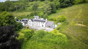 A large, white, two-story house with a spacious front yard, surrounded by lush greenery and hills. - Large modern farmhouse, surrounded by 40 acres of private countryside (Unknown)