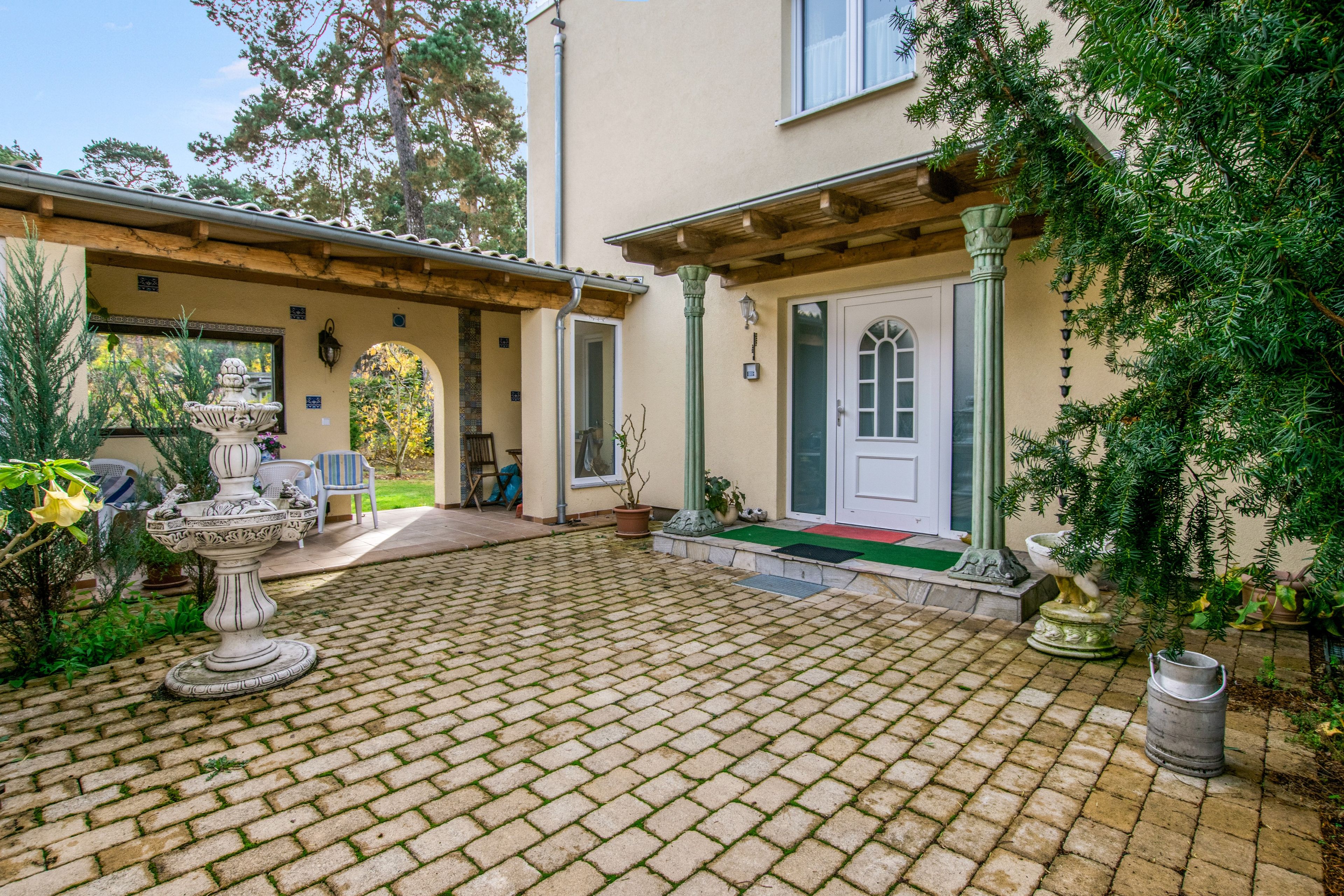 A courtyard with a fountain, a pergola, and a door leading to a covered area.