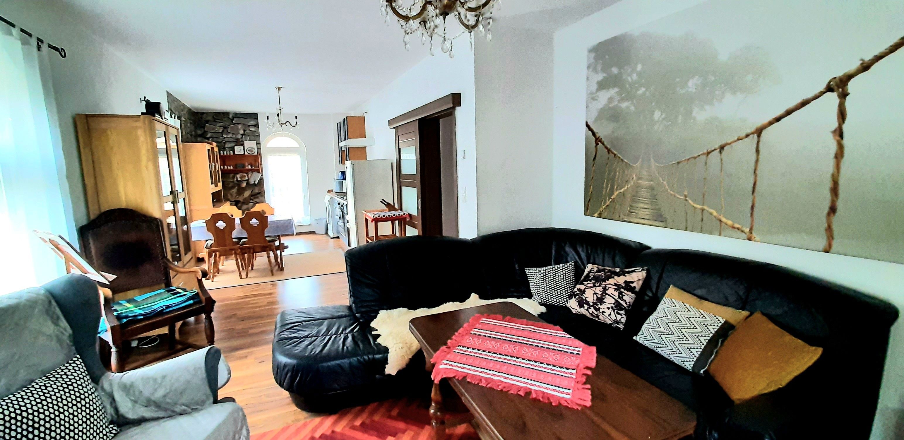 Una sala de estar con un sofá de cuero negro, una mesa de centro de madera y un comedor con mesa y sillas.
