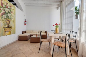 A room with a white brick wall, a large painting, a fire extinguisher, a sofa, a table with chairs, and a window with curtains. - Apartment 'Duna Dorata' with Private Balcony & Relaxation in Torre Lapillo (Porto Cesareo)