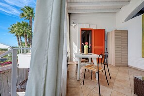 Ein Balkon mit Tisch und Stühlen, eine rote Tür und Blick auf Palmen.