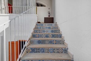 Eine Treppe mit gemusterten Fliesen, weißen Wänden und einem Metallgeländer.
