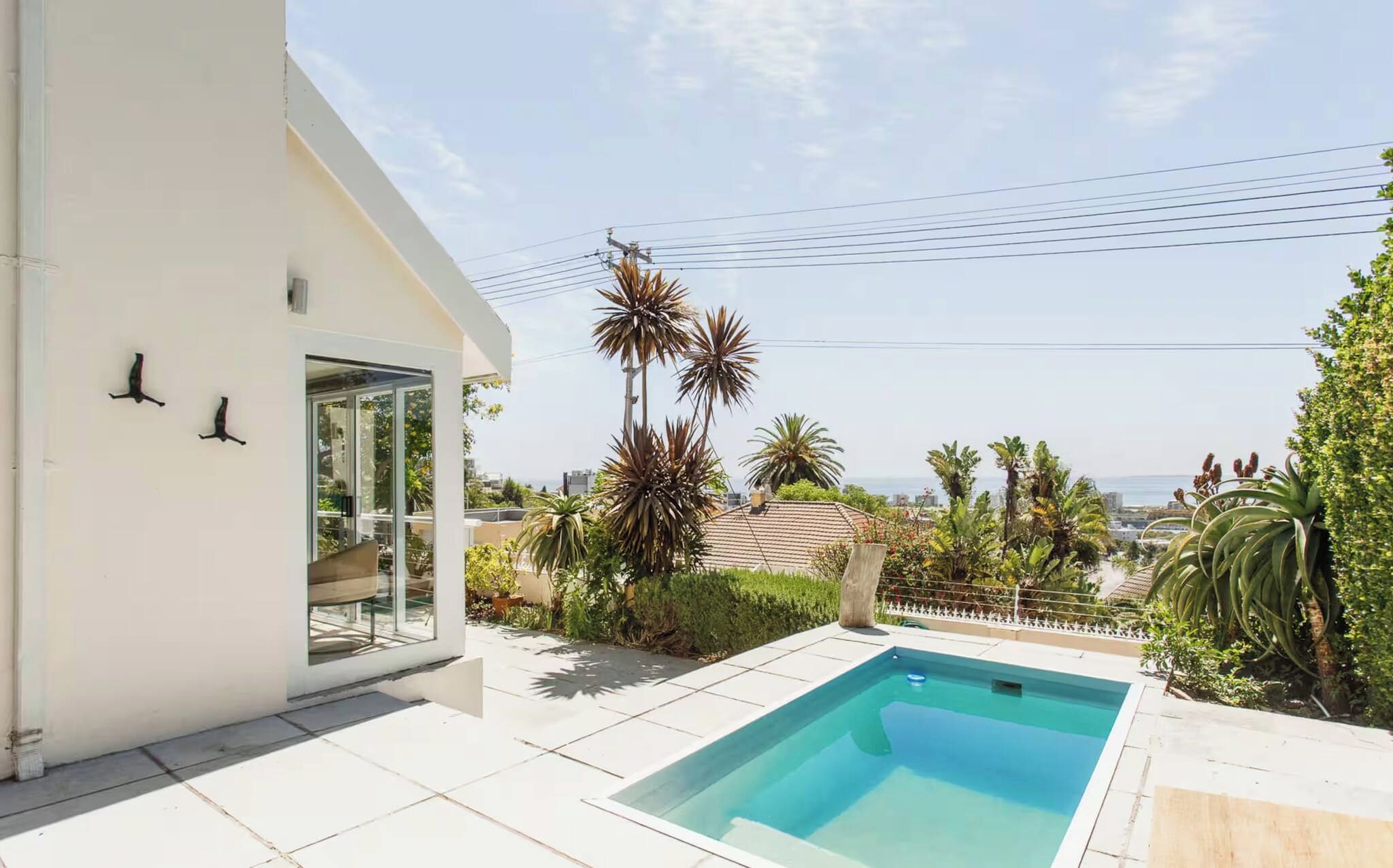 A residential property with a swimming pool, a glass door entrance, and a view of the sea.