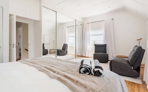 Ein modernes Hotelzimmer mit einem großen Bett, einer Sitzecke mit Stuhl und Sofa, einem Spiegel und Blick ins Freie.