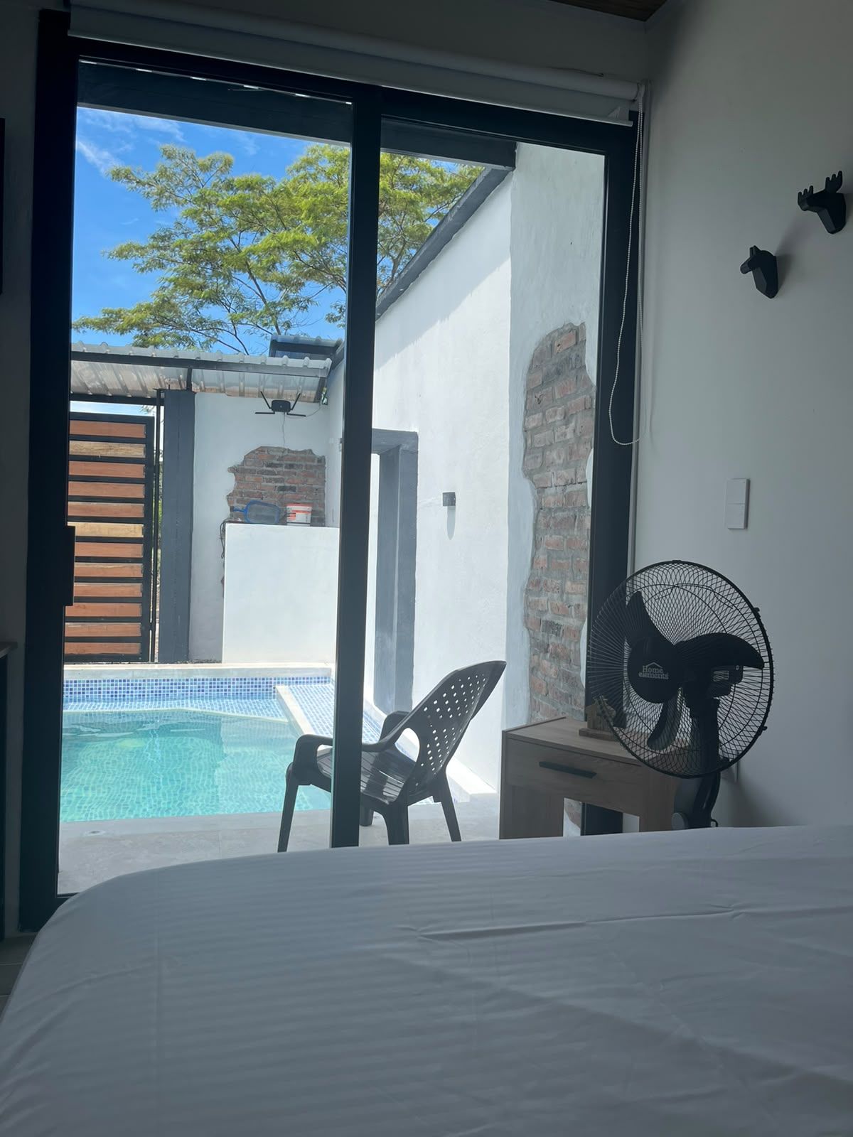 Une chambre avec un lit, un ventilateur, une chaise et une vue sur une piscine.