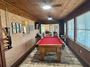 A pool table in a room with brick walls, wooden ceiling, and a window with blinds.