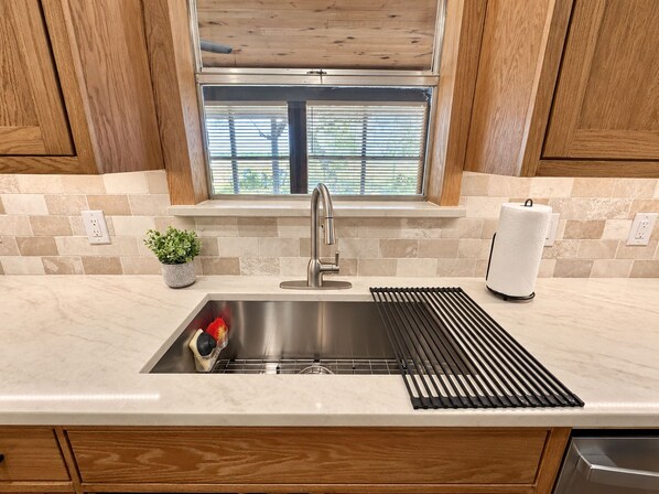 A kitchen with a stainless steel sink, a window with blinds, and a potted plant on the counter.