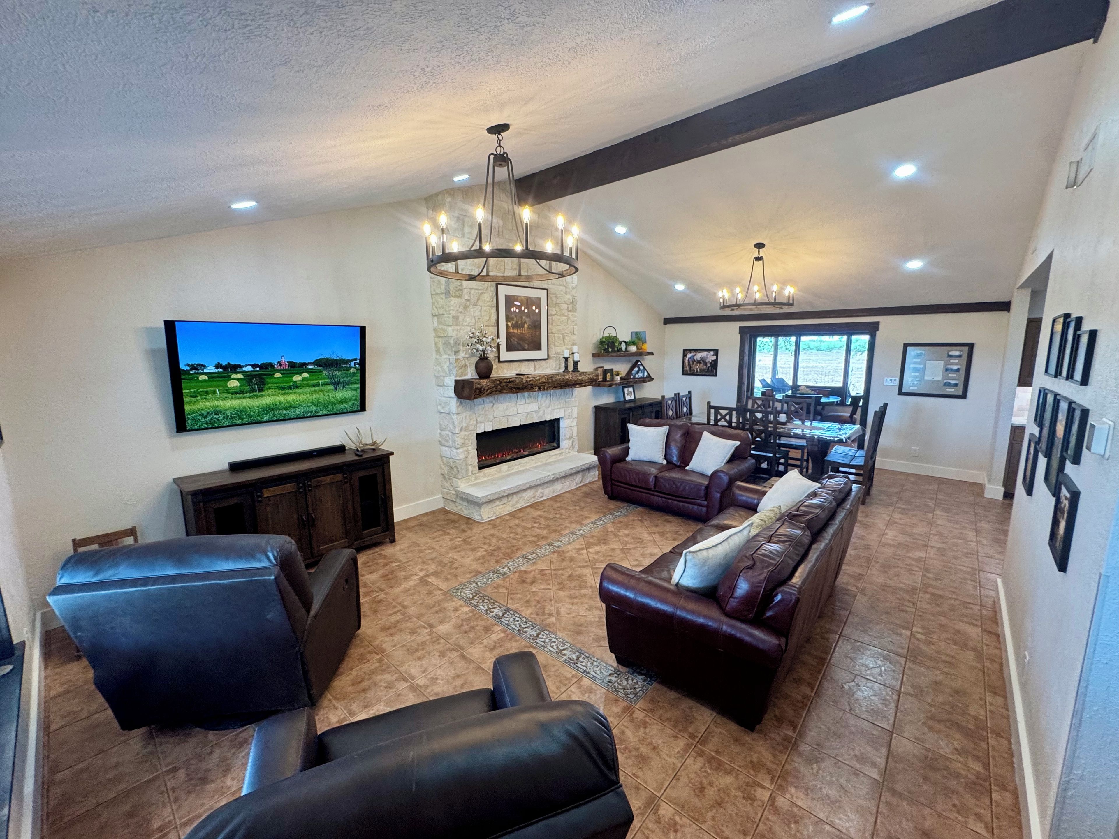 A spacious living room with a fireplace, leather sofas, a television, and a chandelier.