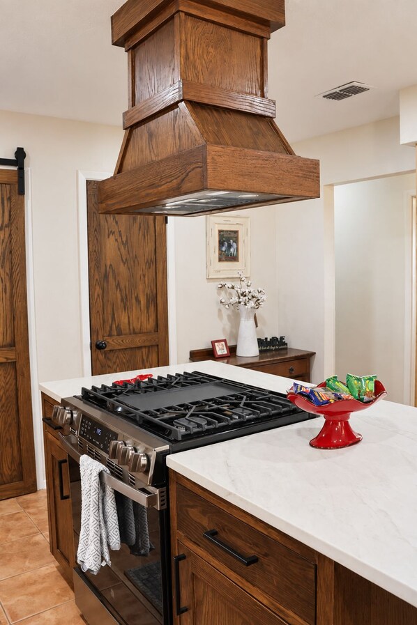 A kitchen with a central island, a stove, and a wooden range hood.