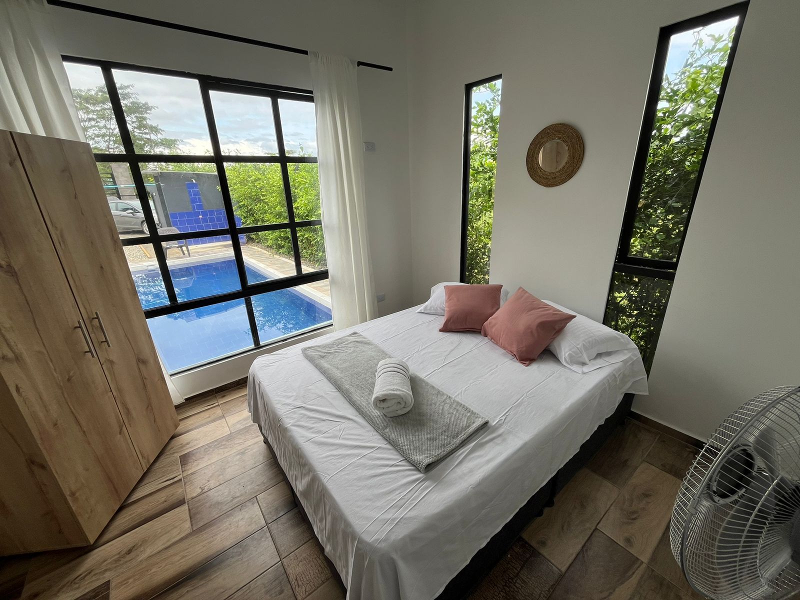 Un dormitorio con cama, almohadas, un ventilador y vista a una piscina.