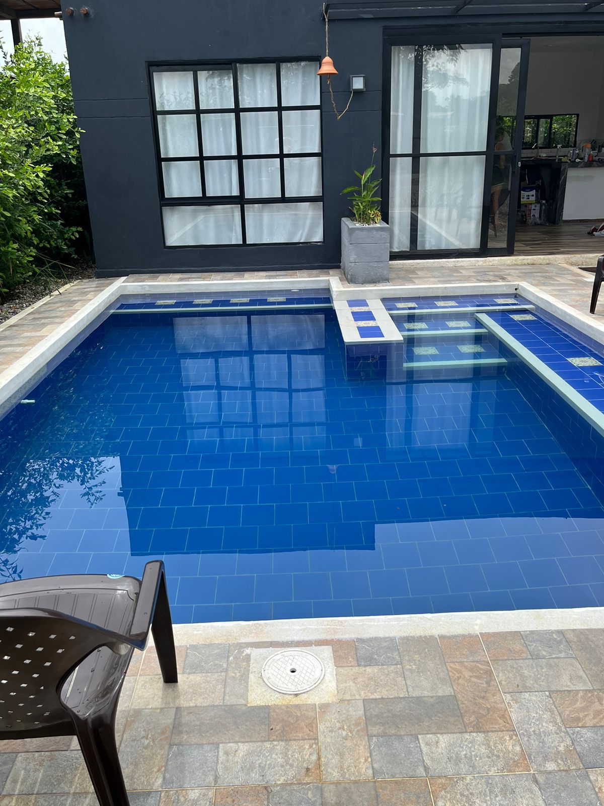 Una piscina rectangular con azulejos azules, rodeada por un patio de piedra.
